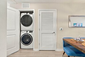 A laundry room with two washing machines, a closed door, a dining table with a blue chair, and a wall-mounted artwork. - Vista Cay 3BR Condo • Pools • Near Universal (Orlando)