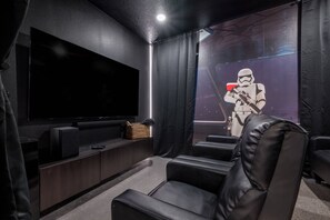 A home theater room with a large flat-screen TV, leather reclining chairs, and a Star Wars-themed wall. - 8BR Themed Villa • Pool, Game Room & Theater (Orlando)