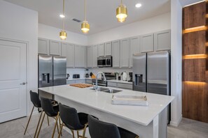 A modern kitchen with stainless steel appliances, a central island with bar stools, and pendant lighting. - 8BR Themed Villa • Pool, Game Room & Theater (Orlando)