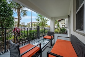 A balcony with outdoor furniture, a glass table, and a view of the surrounding greenery and buildings. - Vista Cay 2BR Condo • King Suite • Near Universal (Orlando)