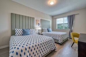Ein Hotelzimmer mit zwei Betten, einem Schreibtisch, einem Stuhl, einem Fenster mit Vorhängen und einer Deckenleuchte.
