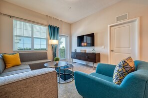 A living room with a sofa, armchair, TV, and a cabinet. - Vista Cay 403 • 3BR Condo, King Suite • Universal (Orlando)