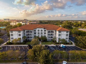A multi-story residential building with a red-tiled roof, surrounded by a parking lot and greenery. - Vista Cay 404 • 3BR Condo, King Suite • Universal (Orlando)