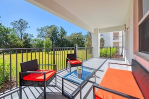 A balcony with outdoor furniture, a glass table, and a view of a green landscape. - Vista Cay 3BR Condo • King Suite • Near Universal (Orlando)