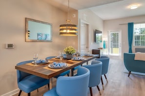 Un coin repas avec une table en bois, des chaises bleues et un luminaire suspendu.