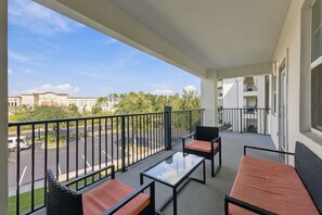 Un balcón con mobiliario exterior, vista despejada a un estacionamiento y un edificio al fondo.