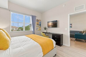 Un dormitorio moderno con cama, escritorio, televisor y vistas al exterior.