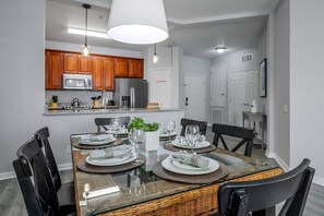 A modern kitchen with wooden cabinets, stainless steel appliances, and a dining area with a glass table set for four. - Vista Cay 3BR Condo • Pools • Near Universal (Orlando)