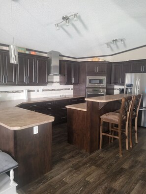 A modern kitchen with dark wood cabinets, stainless steel appliances, and a central island with bar stools. - Spacious family home in Milk River (Milk River)