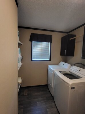 A laundry room with a washing machine, dryer, and shelves with laundry supplies. - Spacious family home in Milk River (Milk River)