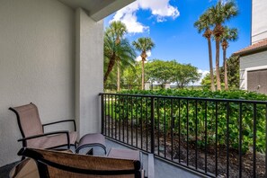 Ein Balkon mit zwei Stühlen und einem kleinen Tisch, mit Blick auf einen Garten mit Palmen und blauem Himmel.