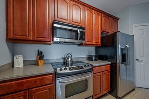A kitchen with wooden cabinets, a stainless steel microwave, a refrigerator, a stove, and a toaster. - Vista Cay 3BR Condo • King Suite • Near Universal (Orlando)