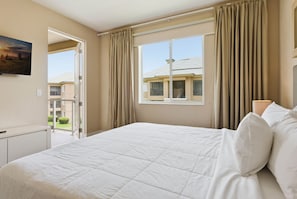 A hotel room with a bed, a desk, a window with curtains, and a view of neighboring buildings. - 3 Suites • Private Hot Tub • Near Disney (Kissimmee)