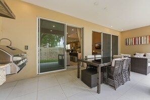 A patio area with a grill, wicker furniture, and a sliding glass door leading to a kitchen. - 3 Suites near Disney • Patio Grill & Balcony (Kissimmee)