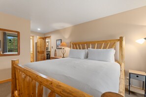 Un lit en bois avec des draps blancs, dans une pièce aux murs de couleur beige et dotée d’une tête de lit en bois.