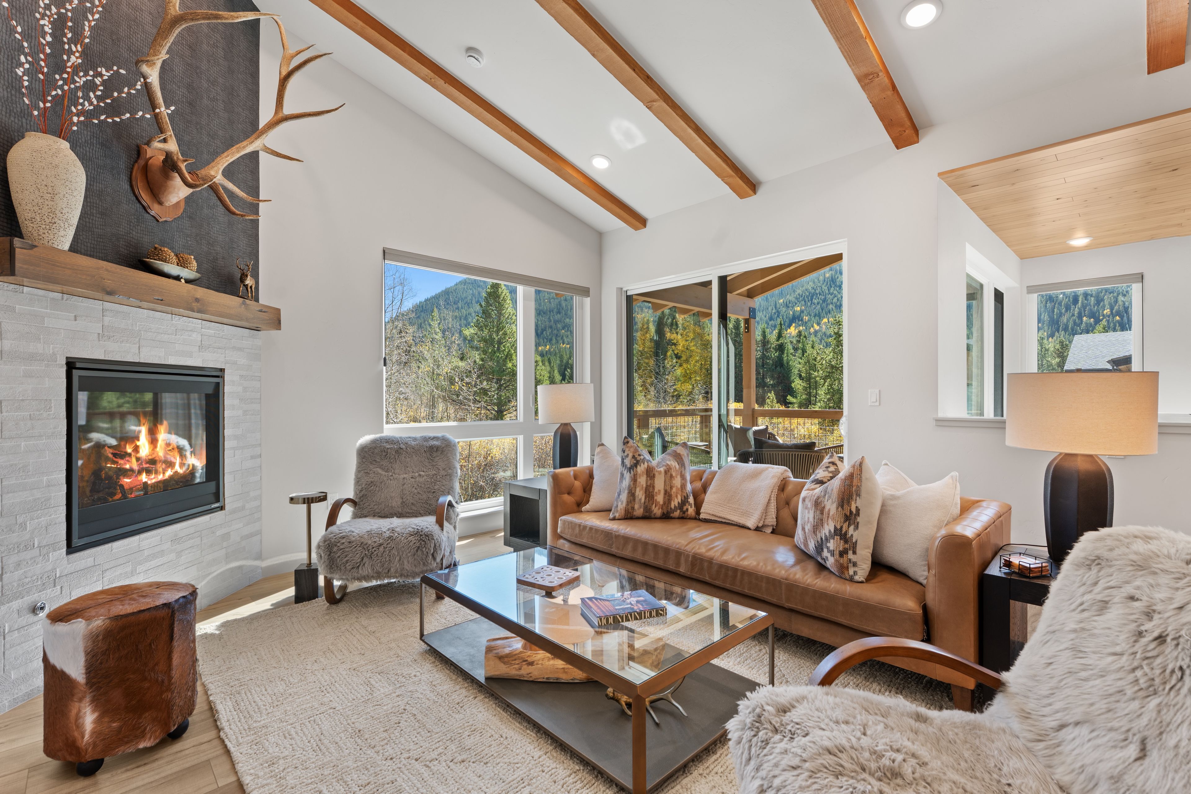 A spacious living room with a fireplace, leather sofa, and large windows offering mountain views.