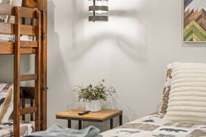 A bedroom with a wooden ladder, a bedside table with a remote control, a potted plant, and a bed with patterned bedding. - Walk to Snow Summit Condo | Hot Tub | Fireplace (Big Bear Lake)