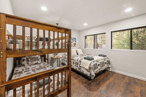 Une chambre avec deux lits, un berceau en bois et une fenêtre avec des stores.