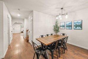 Un coin repas avec une table en bois et des chaises noires, un escalier et un couloir menant à une autre pièce.