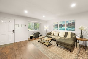 A living room with a sofa, coffee table, and artwork on the wall. - Walk to Snow Summit Condo | Hot Tub | Fireplace (Big Bear Lake)