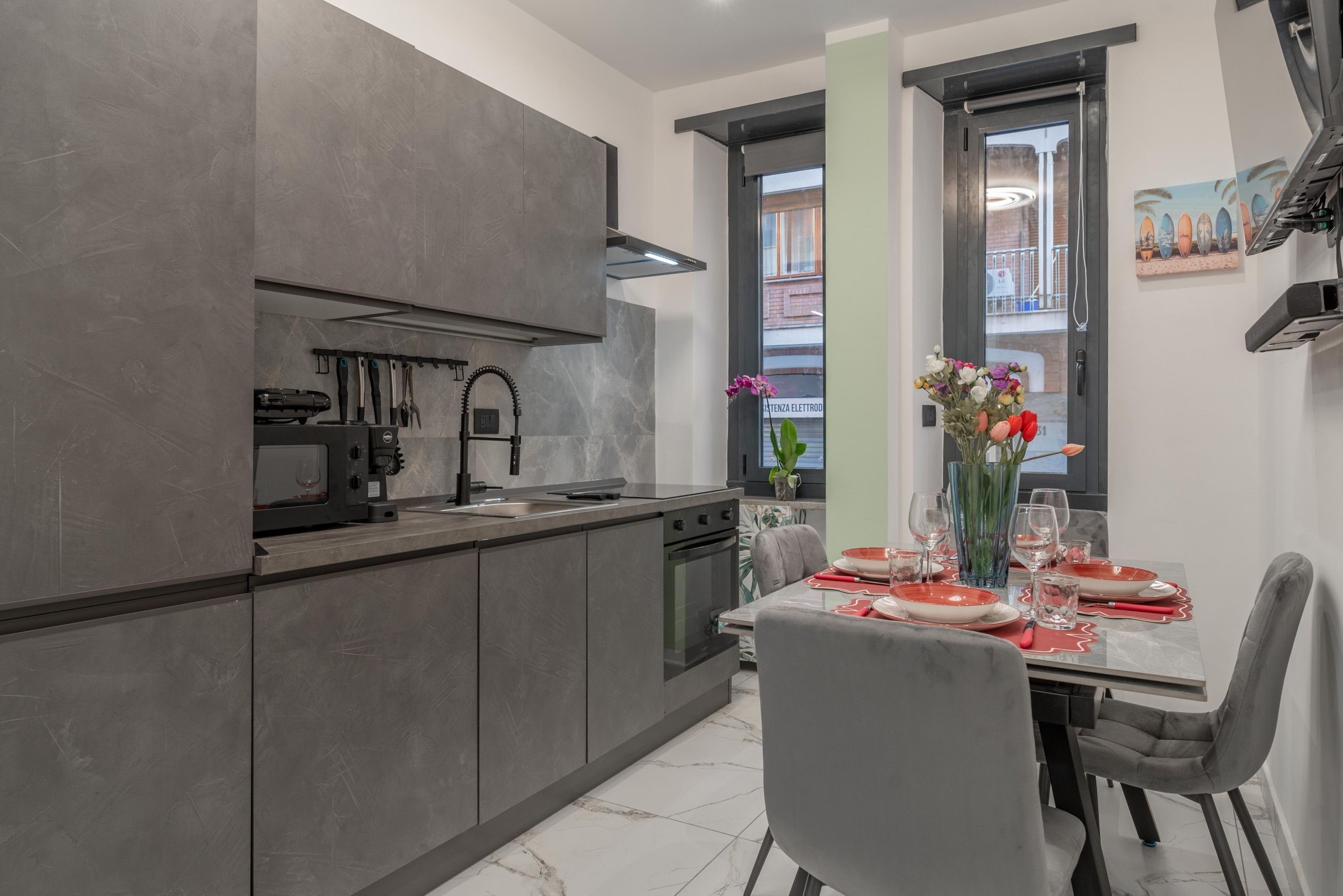 Una cocina moderna con armarios grises, horno empotrado y un comedor con mesa dispuesta para dos.