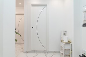 Un couloir avec une porte blanche, un radiateur et un petit meuble blanc avec des tiroirs.