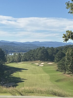 Un campo de golf con vistas despejadas del paisaje circundante, incluyendo colinas lejanas y un cuerpo de agua.