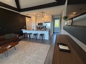 A modern kitchen with a central island, bar stools, and a dining area with a sofa and coffee table. - Currahee Club Spacious 2BR Condo • Golf, Lake and Mountain Retreat (Toccoa)