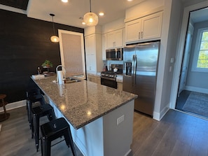 A modern kitchen with a granite countertop, stainless steel appliances, and a black backsplash. - Currahee Club Spacious 2BR Condo • Golf, Lake and Mountain Retreat (Toccoa)