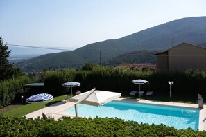 A swimming pool with lounge chairs and umbrellas, surrounded by greenery and a mountainous backdrop. - The Bauhaus Room - Lucca Countryside (Lucca)