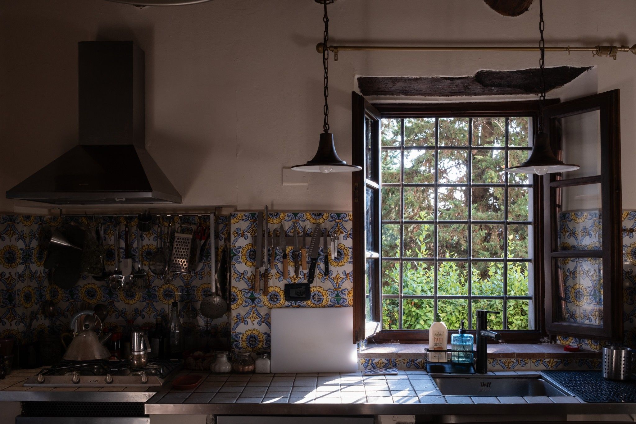 Una cucina con un fornello, utensili da cucina appesi e una finestra vista su del verde.