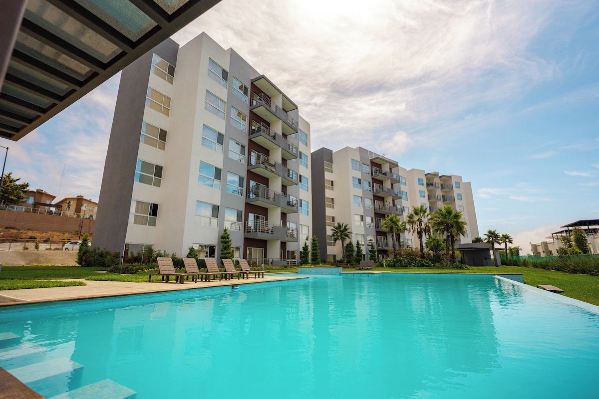 Un moderno edificio de apartamentos con piscina, balcones y cielo despejado.