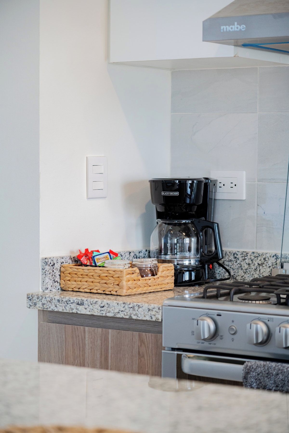 Una cocina con estufa a gas, cafetera y una cesta de aperitivos en la encimera.