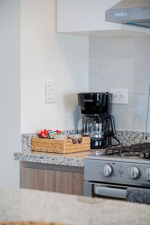 A kitchen with a gas stove, a coffee maker, and a basket of snacks on the counter. - Apartament 3Bd Amaralta (Playas de Rosarito)
