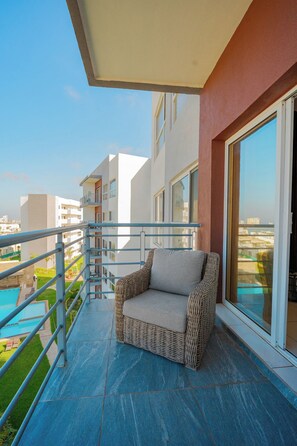 A balcony with a wicker chair, a pool, and a view of other buildings. - Apartament 3Bd Amaralta (Playas de Rosarito)