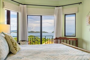 A bedroom with a large bed, two windows with curtains, a view of the sea, and a small table. - Ocean View Villa - Infinity Pool & Near Beaches (Potrero)