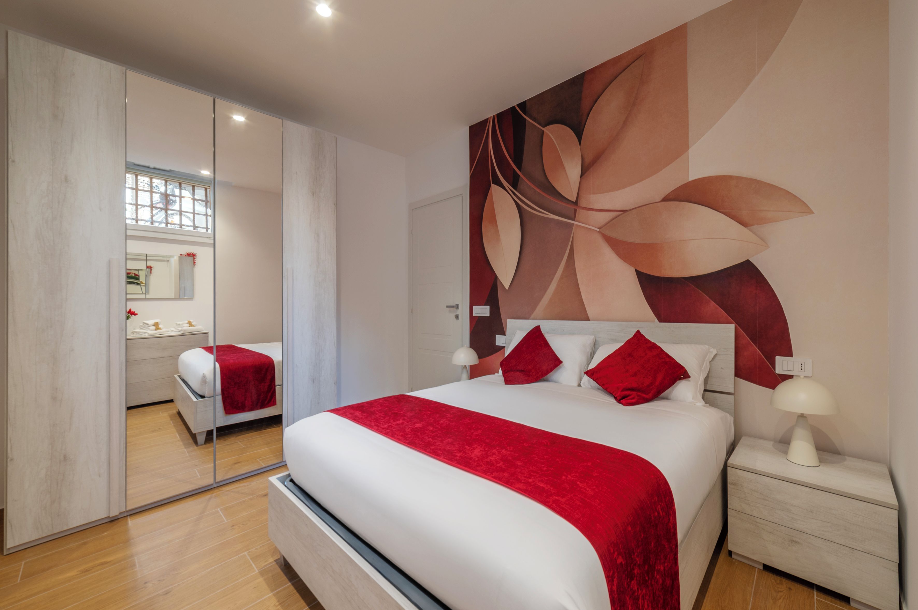 A modern bedroom with a large bed, a nightstand, a mirror, and a wall with a leaf design.