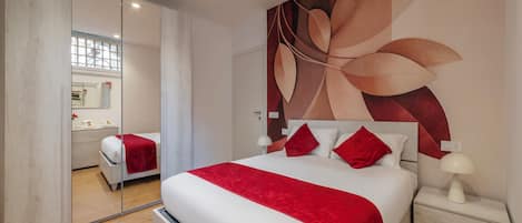 A modern bedroom with a large bed, a nightstand, a mirror, and a wall with a leaf design.