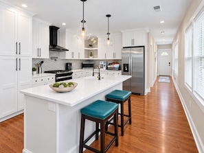 A modern kitchen with white cabinetry, a stainless steel refrigerator, a large island with stools, and pendant lighting. - Atlanta Ranch Retreat 6BR - Sleeps 16 (Atlanta)