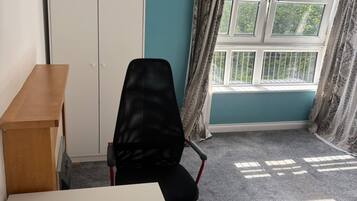 Une pièce aux murs de couleur turquoise, avec un bureau blanc, une chaise de bureau noire, une armoire et une fenêtre avec des rideaux.