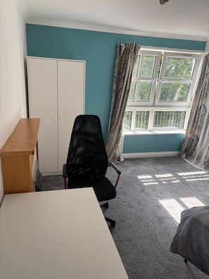 A room with teal walls, a white desk, a black office chair, a wardrobe, and a window with curtains. - Spectrum (Edinburgh)