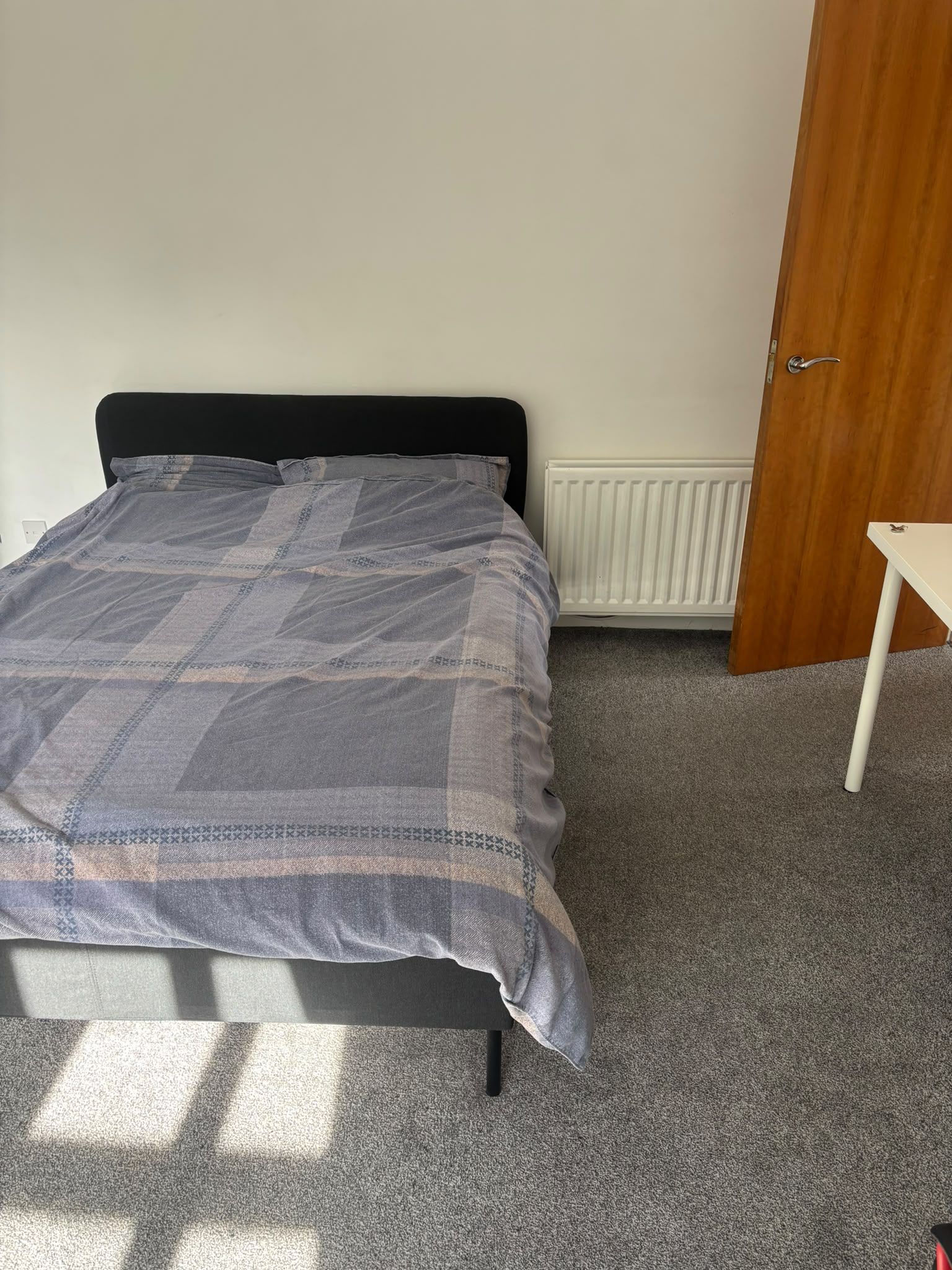 A bedroom with a bed, a radiator, a wooden door, and a small table.