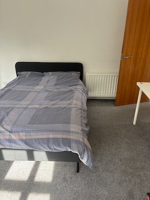 A bedroom with a bed, a radiator, a wooden door, and a small table. - Spectrum (Edinburgh)