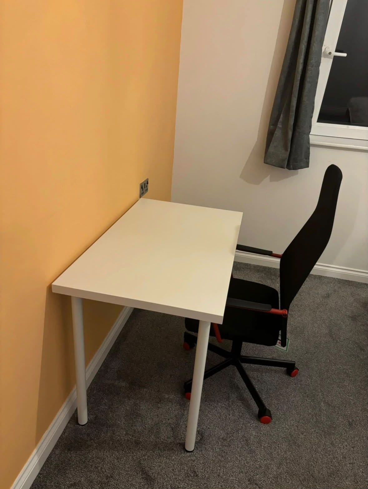 A small room with a white table and a black office chair with red accents.