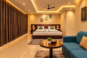 A modern hotel room with a large bed, a sofa, a round coffee table, and a ceiling fan. - Hotel Corporate Inn (Guwahati)