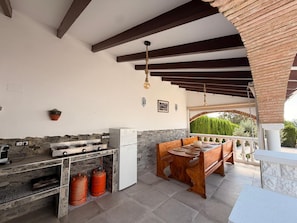 Un espace cuisine extérieur avec un mur en pierre, un banc en bois et une cuisinière à gaz.