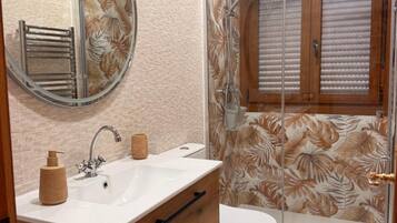 Een badkamer met een houten wastafelmeubel, een ronde spiegel, een douche met glazen deur en een toilet.