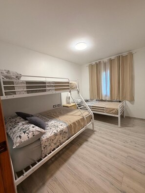 Une chambre avec deux lits superposés, une table de chevet, une lampe et une fenêtre avec des rideaux.