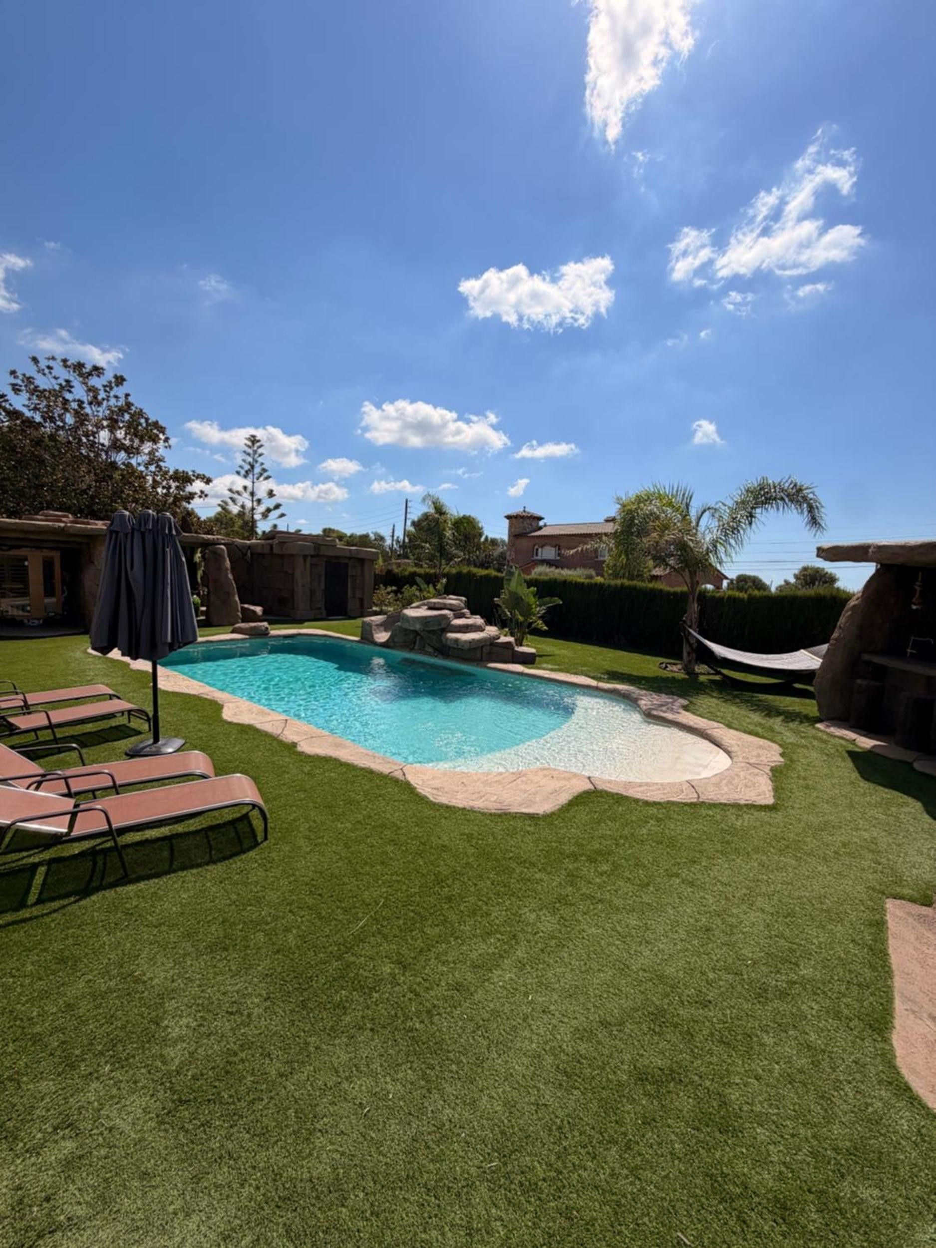 Un jardin avec une piscine, du gazon synthétique et un hamac.