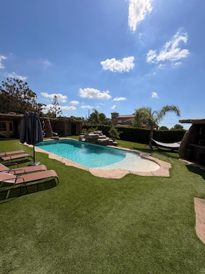 Un jardin avec une piscine, du gazon synthétique et un hamac.